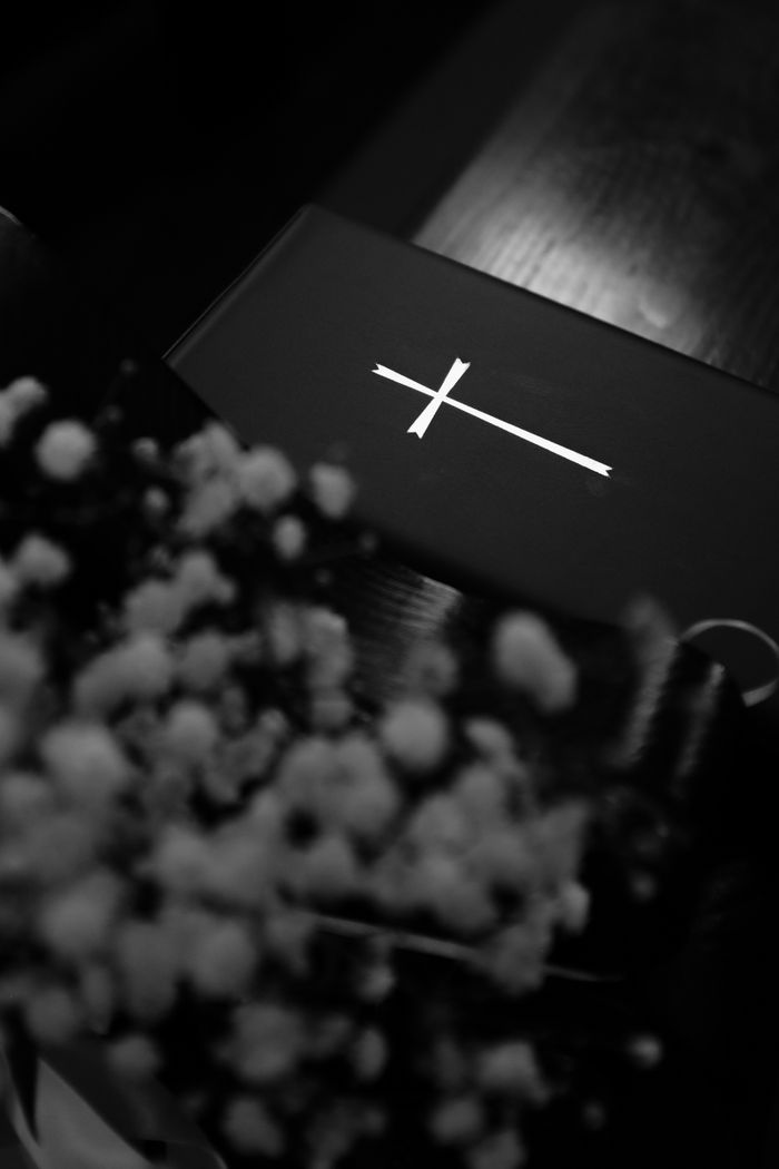 The Art of Drawing Readers In: Your attractive post title goes here A monochrome image featuring a cross on a Bible with blurred flowers in the foreground.